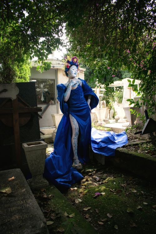Free A woman in an elegant blue gown poses artistically in a lush, overgrown cemetery in Mexico City. Stock Photo