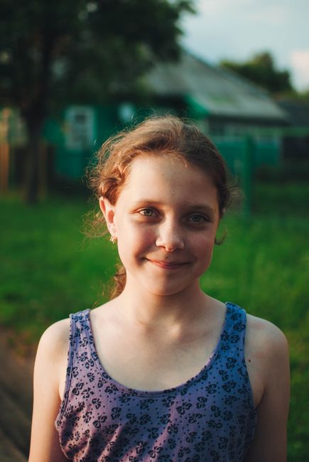 Portrait of a smiling girl outdoors under soft, evening summer light.