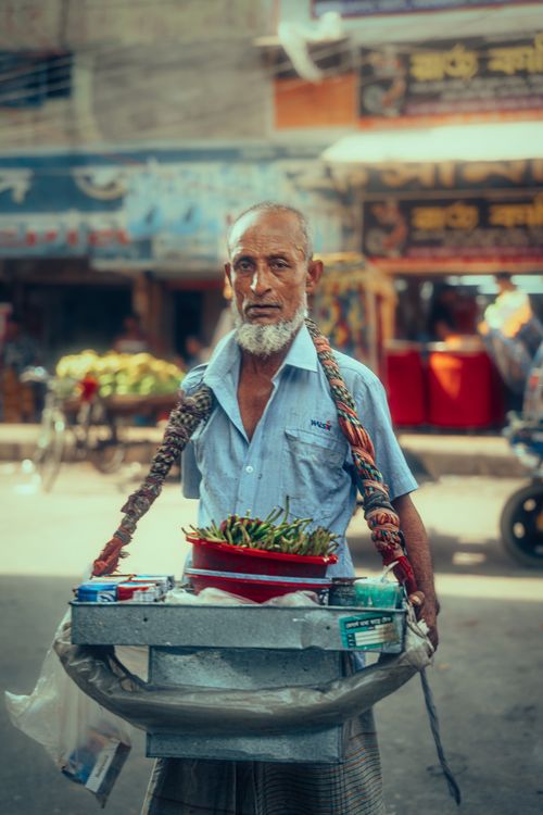 Free Older man selling fresh vegetables in a bustling street market. Vibrant street life captured. Stock Photo