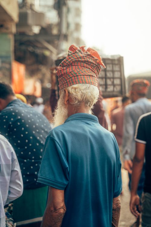 Free An elderly man with a plaid turban walks through a crowded urban street, capturing street life. Stock Photo