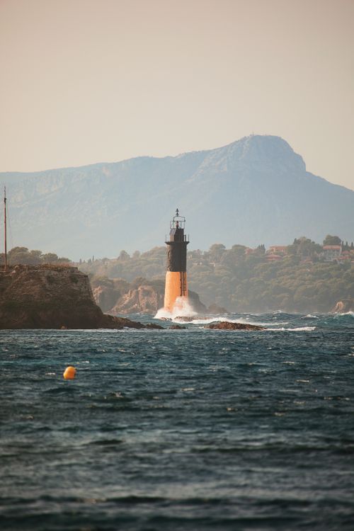 Free Dramatic view of a lighthouse on the rocky coast of Hyères, with mountains in the background. Stock Photo