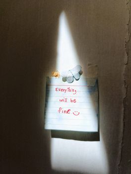 A note stating 'Everything will be fine' lit by a soft beam of light on a wall.