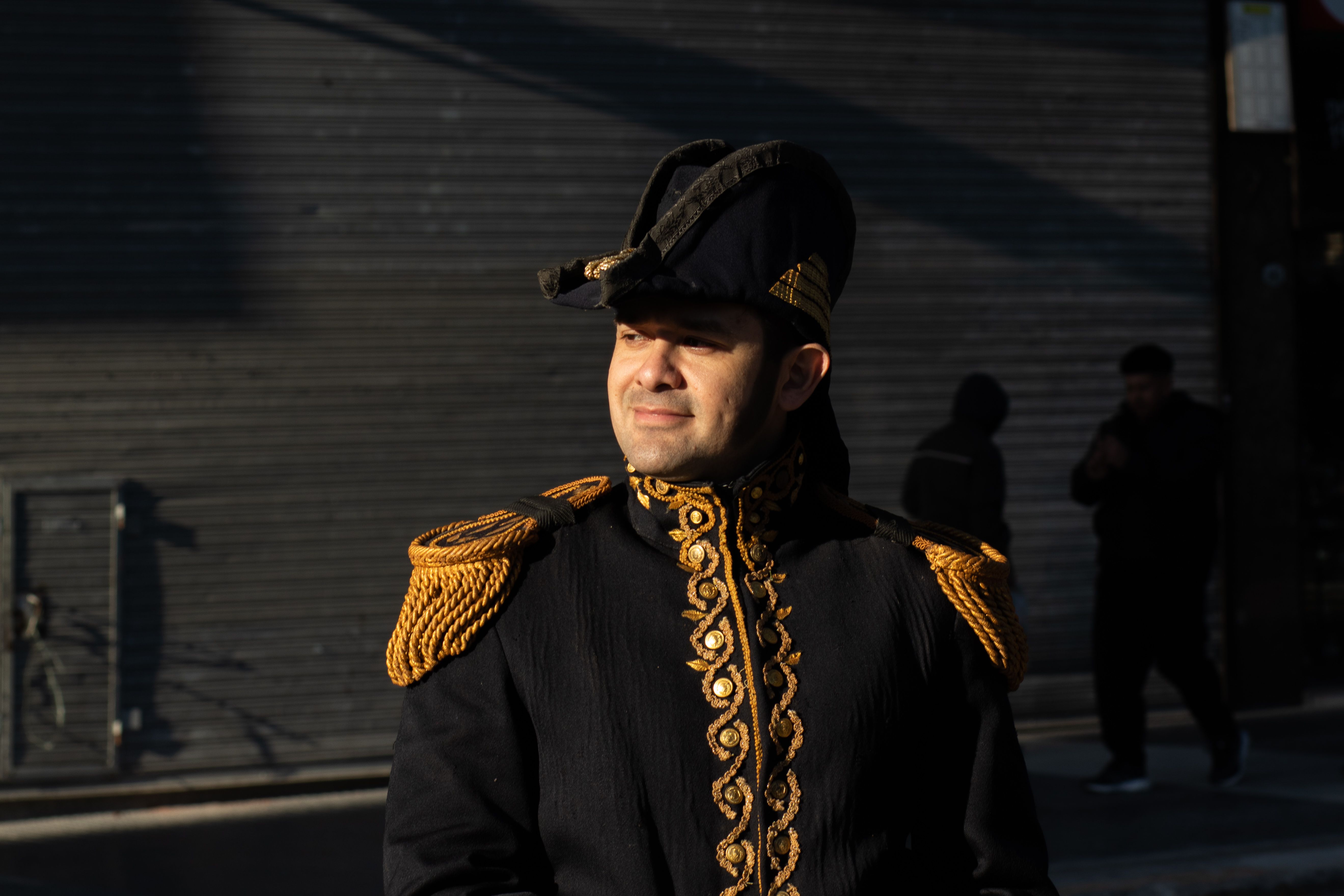 A man in a detailed historical costume basks in sunlight against an urban backdrop.