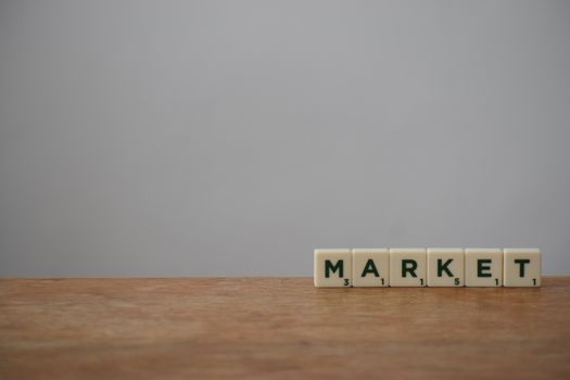 Scrabble tiles spelling 'Market' on a wooden table with a minimalist background.