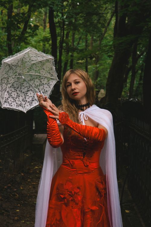 Free A woman in a gothic red dress holding a lace parasol in a forest setting. Stock Photo