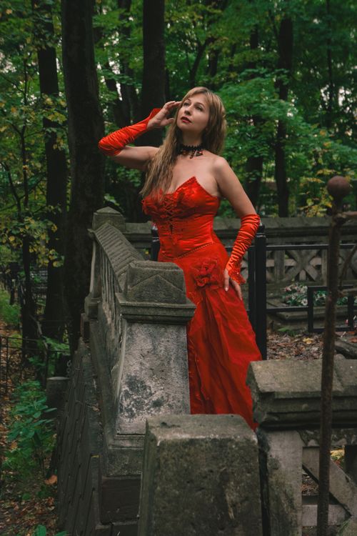 Free Elegant woman in a striking red dress poses gracefully in a lush forest setting. Stock Photo