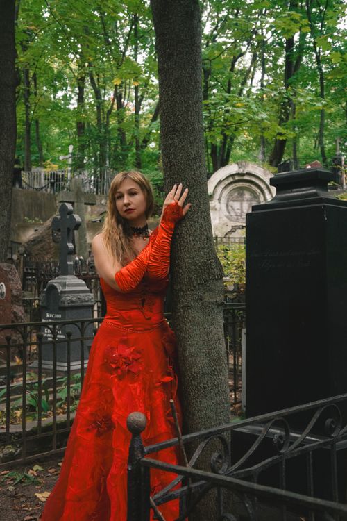 Free Elegant woman in a red gown standing in a historic cemetery surrounded by tombstones. Stock Photo