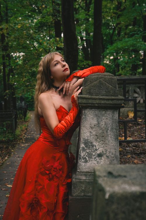 Free A woman in a vibrant red dress poses elegantly outdoors in a lush forest setting during daytime. Stock Photo