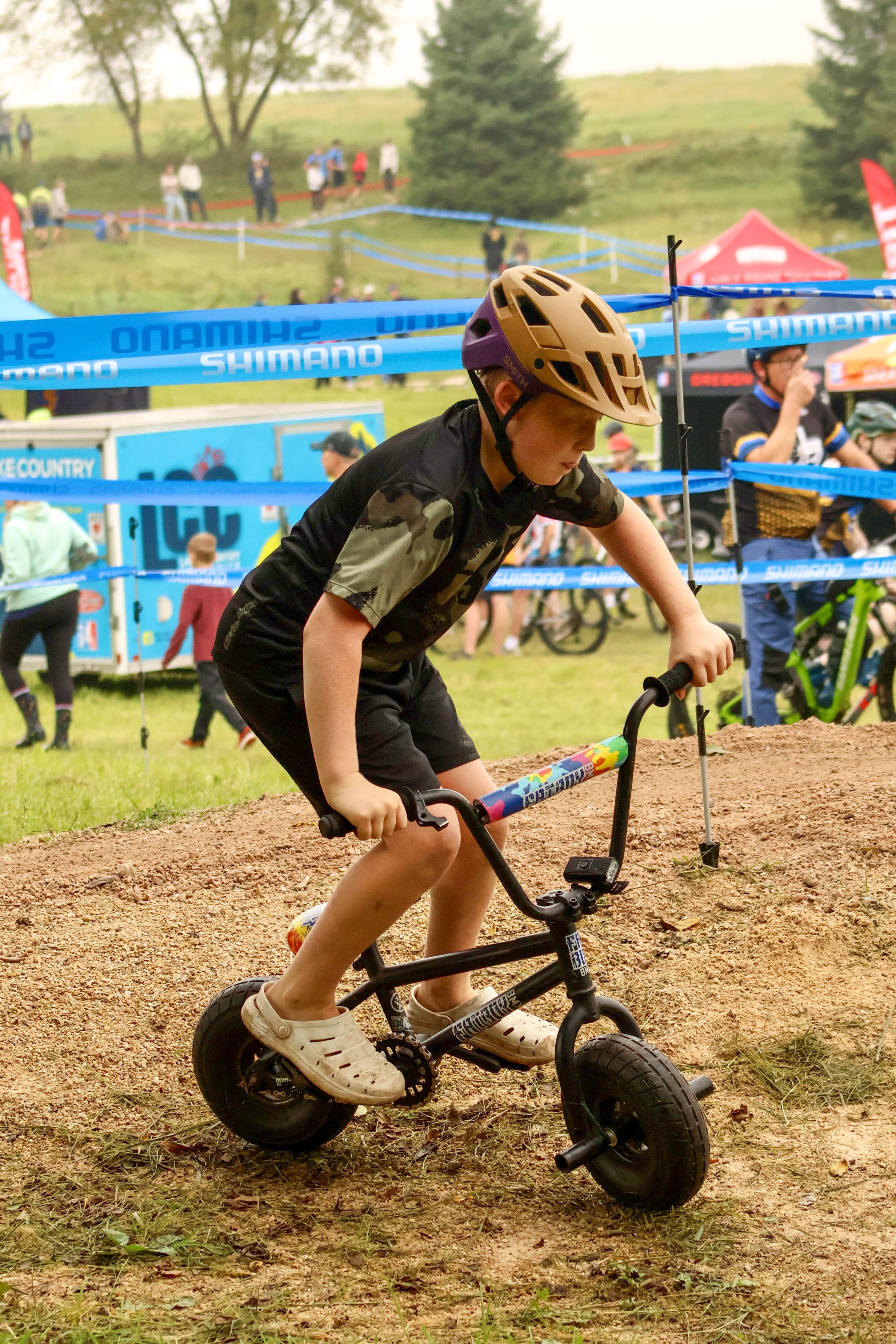 A child enjoys a balance bike ride at an outdoor cycling event in a grassy area.