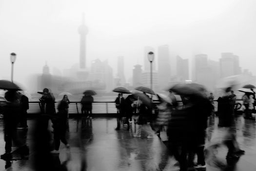 Blurred pedestrians with umbrellas on a rainy day in Shanghai's Bund area.
