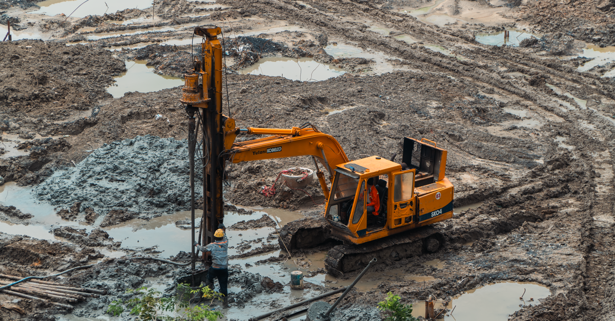 An excavator and worker on a muddy construction site showing industrial equipment.