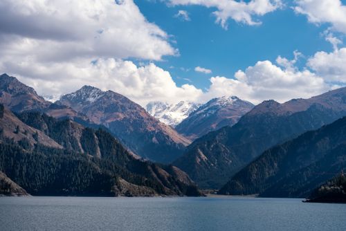 Free Stunning view of snow-capped mountains with a tranquil lake reflecting under a bright blue sky. Stock Photo
