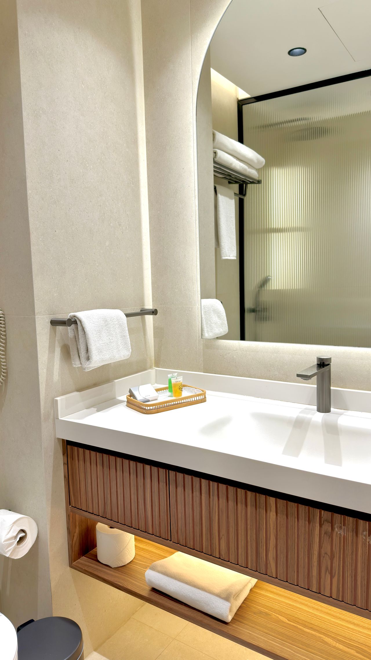 Modern minimalist bathroom vanity with folded towels, amenity tray, and toilet paper