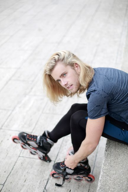 Blonde man tightening roller skates. Casual street style and leisure activity.