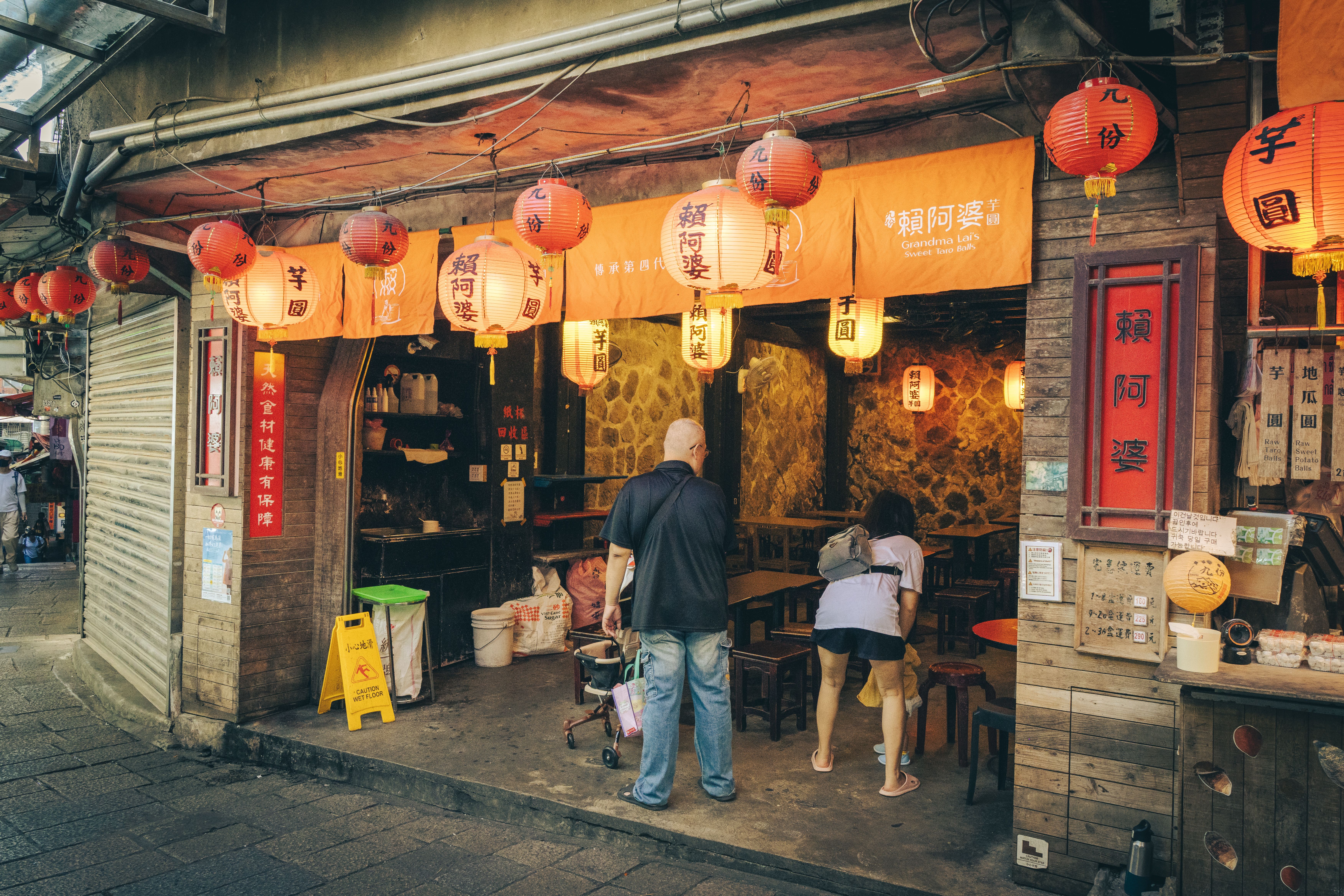 Cozy Asian street food shop illuminated by red lanterns, inviting atmosphere with people outside.