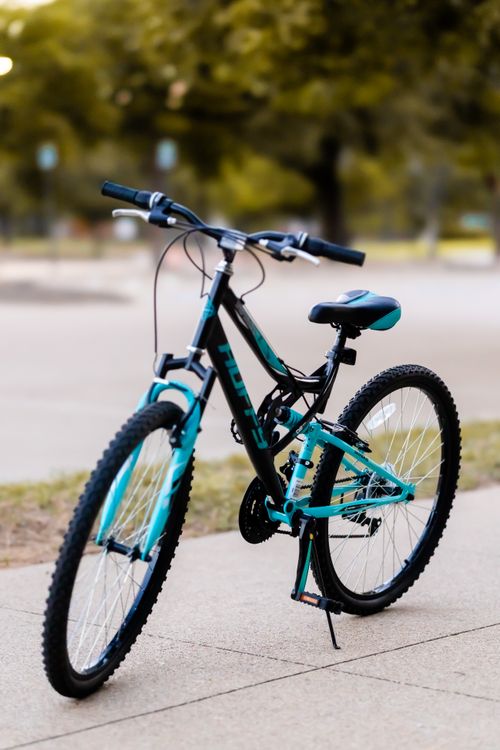 Free A sleek blue mountain bike parked on a sidewalk with greenery in the background. Stock Photo