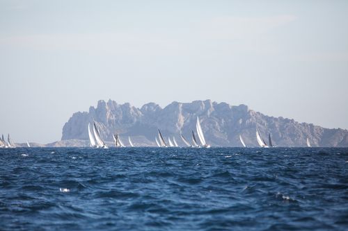 Free Distant sailboats race in the vibrant blue waters off Marseille with rocky cliffs in view. Stock Photo
