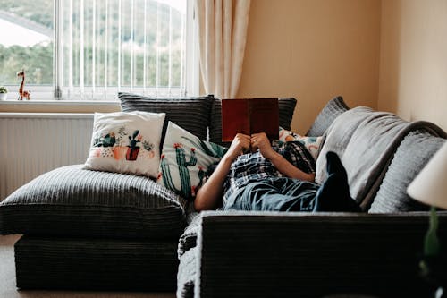 무료 책을 읽고 소파에 누워있는 사람 스톡 사진