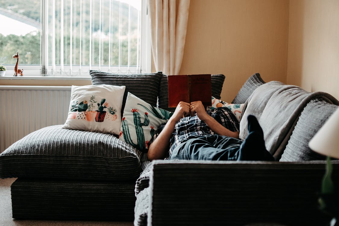 Free Person Lying on Couch Reading a Book Stock Photo