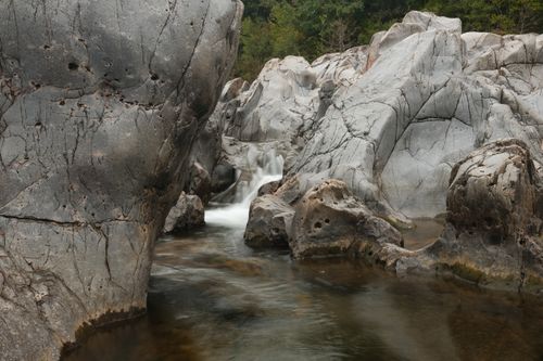 Free A tranquil scene of a rocky gorge with a gentle stream flowing through, surrounded by lush greenery. Stock Photo