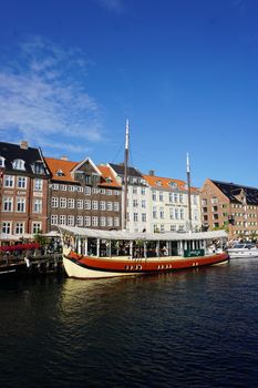 Traditional ship docked at colorful Nyhavn harbor in Copenhagen, Denmark, under a clear blue sky.