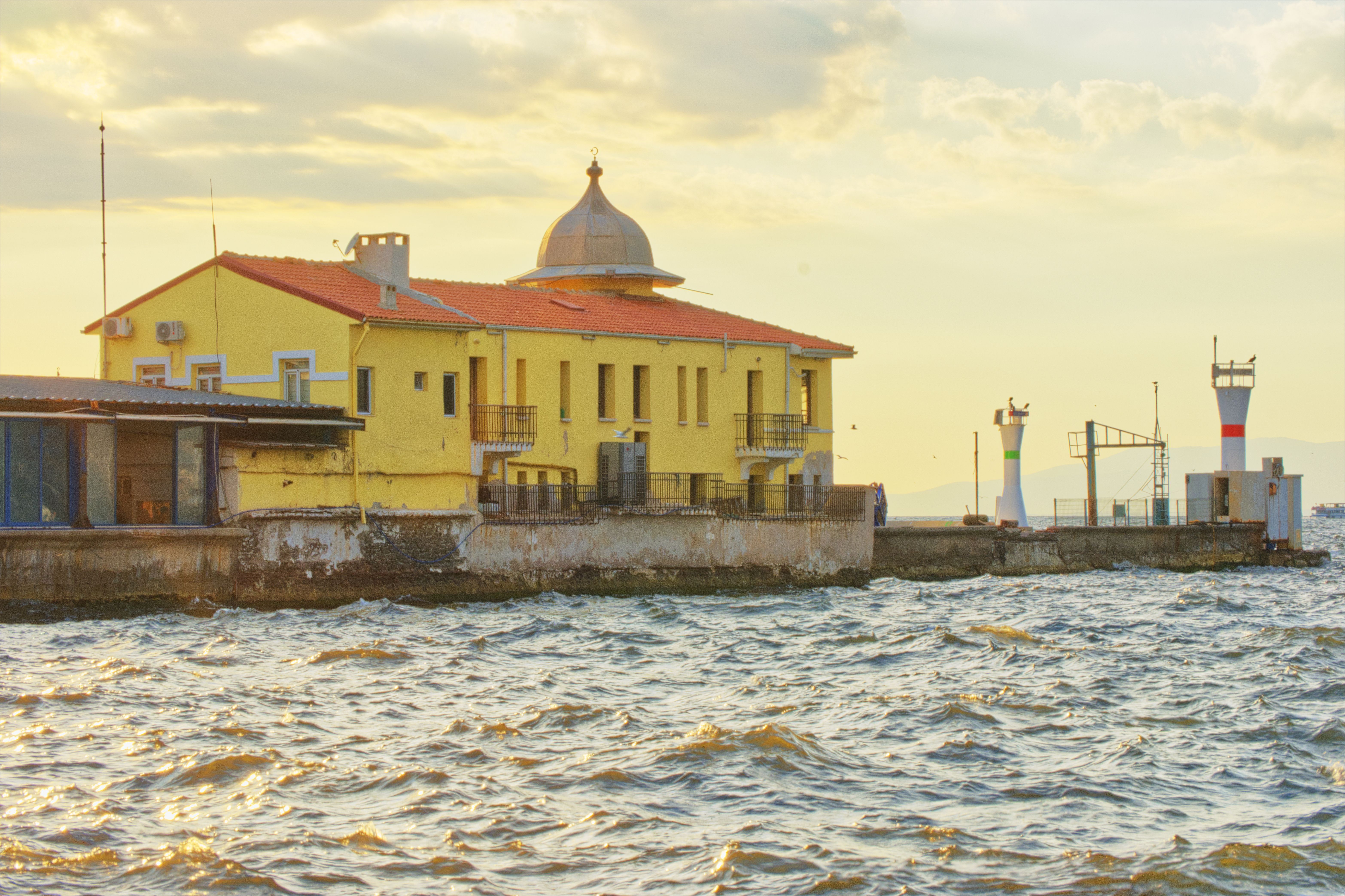 Golden hour view of the historic yellow building at Pasaport Pier, İzmir, Türkiye with choppy seas.
