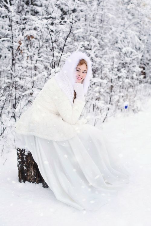 Free Woman in white winter clothing sitting in snowy forest setting, conveying elegance and tranquility. Stock Photo