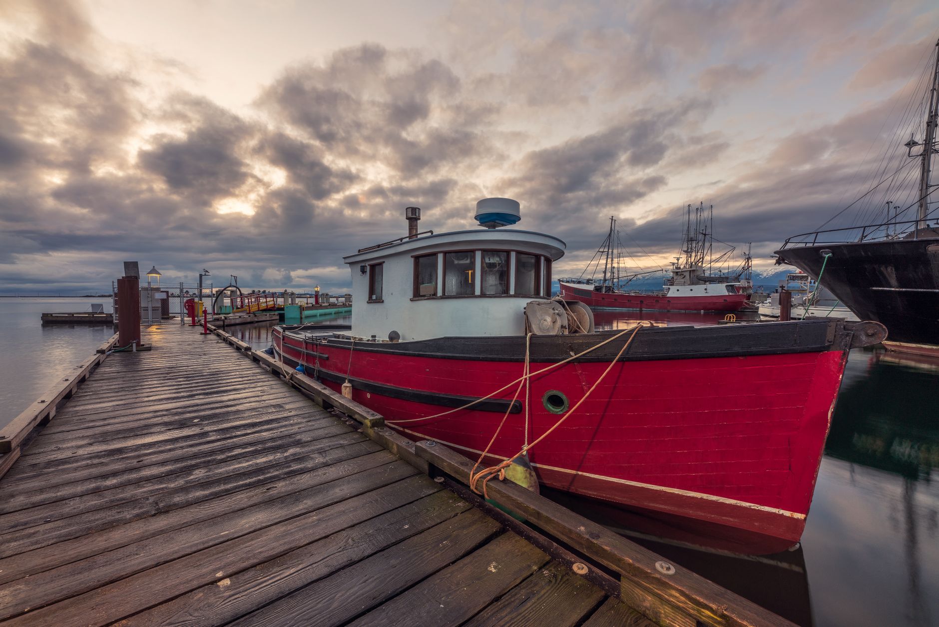 Red fishing boat docked at Comox Marina, BC during a dramatic sunset.