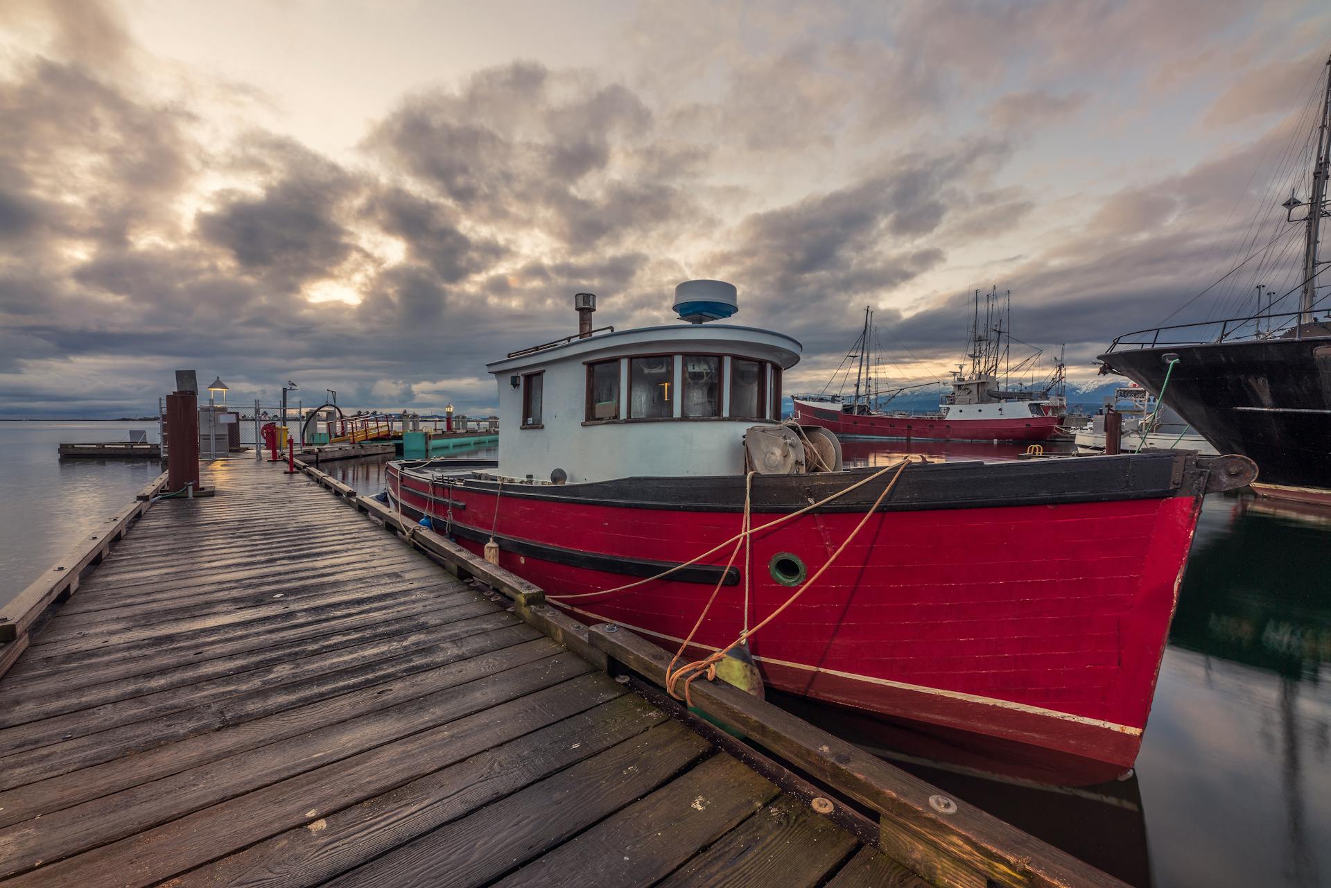 Red fishing boat docked at Comox Marina, BC during a dramatic sunset.