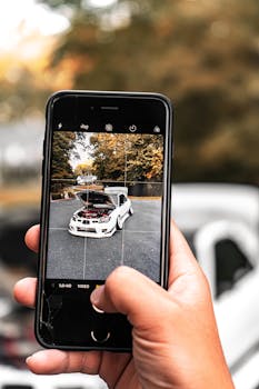 Person photographing a white car outdoors with a smartphone, showing technology and leisure.