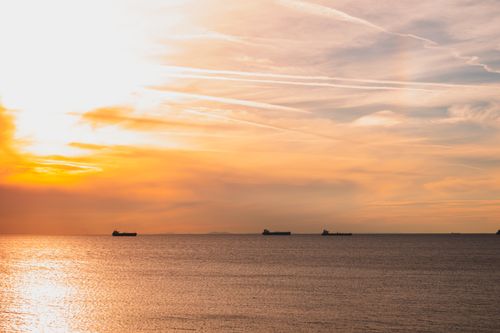 Free Peaceful sunset scene with ships on a calm ocean under a vibrant sky. Stock Photo