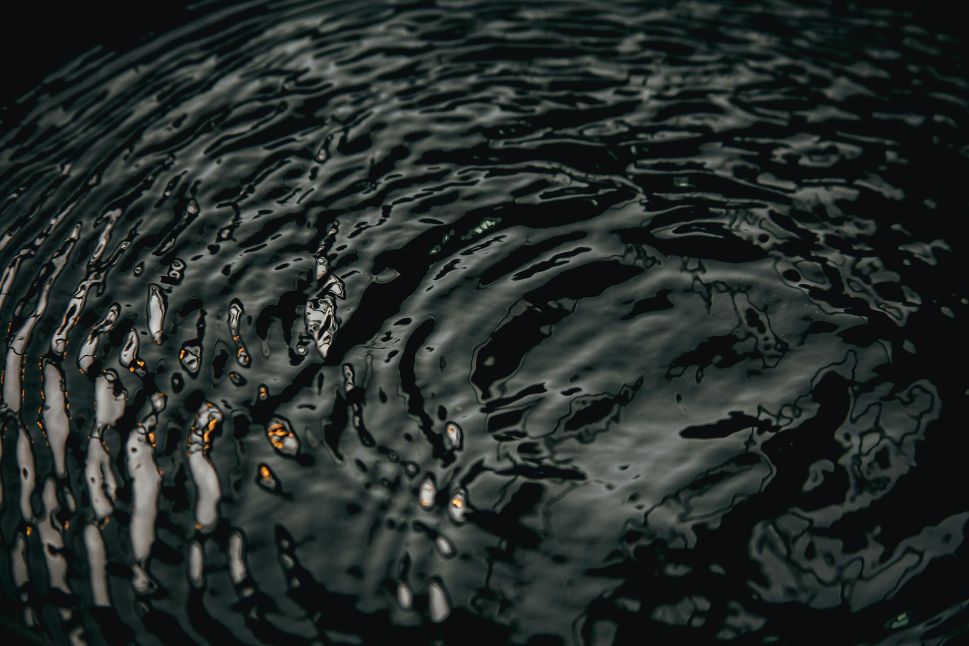 Close-up of dark water ripples reflecting light, creating a moody texture.