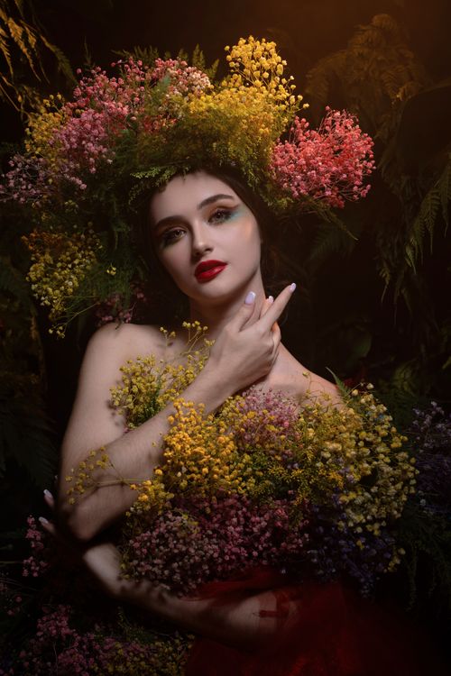 Free A captivating portrait of a woman adorned with vibrant flowers, set against a dark background. Stock Photo