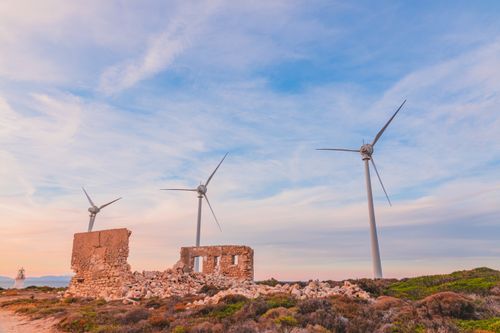 Free Scenic view of wind turbines beside ancient ruins under a colorful sunset sky, symbolizing renewable energy and heritage. Stock Photo