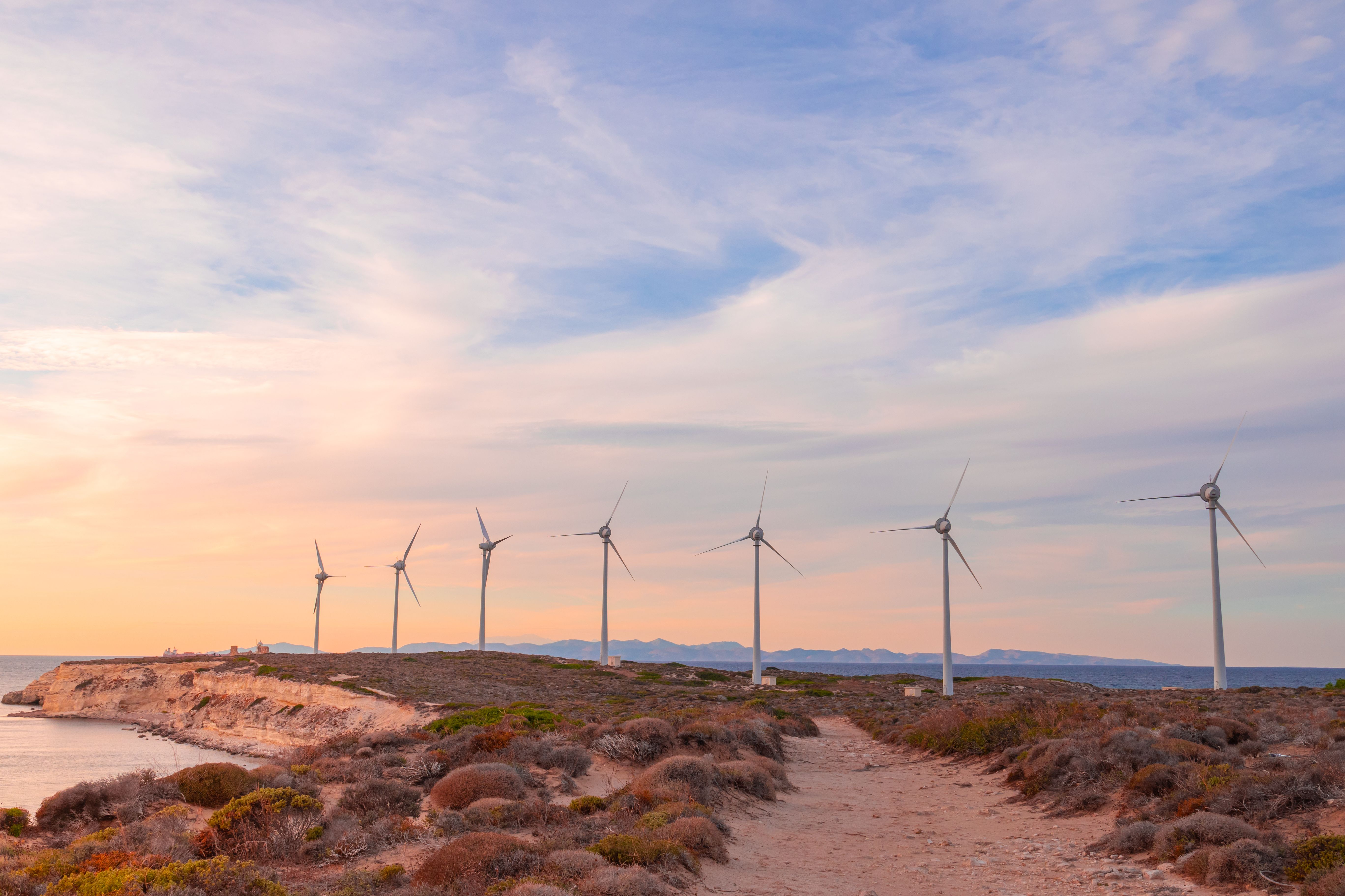 Fotomural Vista panorámica de aerogeneradores a lo largo de un paisaje costero al atardecer, promoviendo las energías renovables.