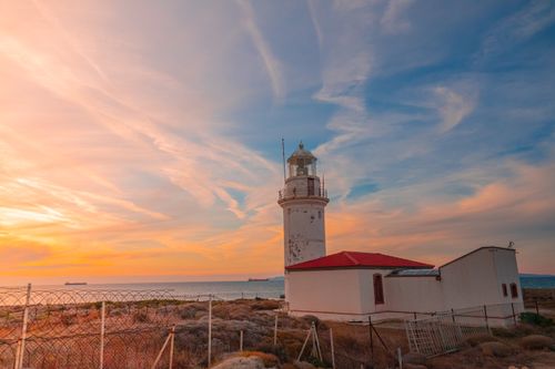 Free A lighthouse by the sea at sunset, under a colorful sky. Perfect for travel and nature photography. Stock Photo