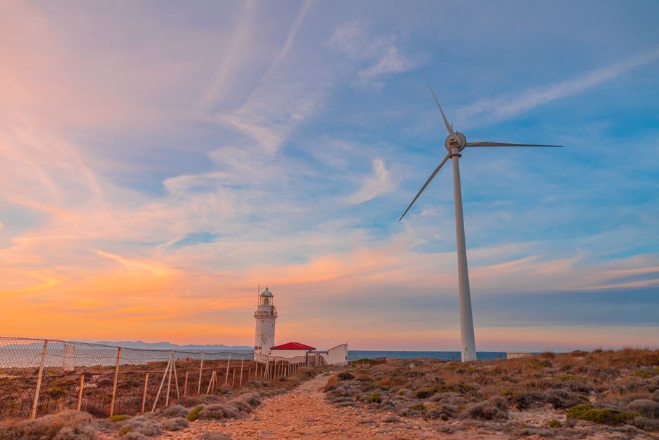 Fotomural Una imagen serena de un aerogenerador y un faro junto a la costa al atardecer, que pone de relieve la energía renovable.