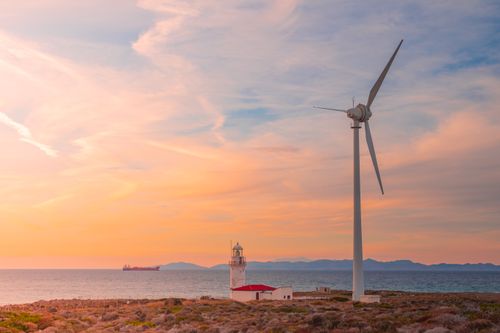 Free Stunning sunset over a coastal landscape with a wind turbine and lighthouse, symbolizing renewable energy. Stock Photo
