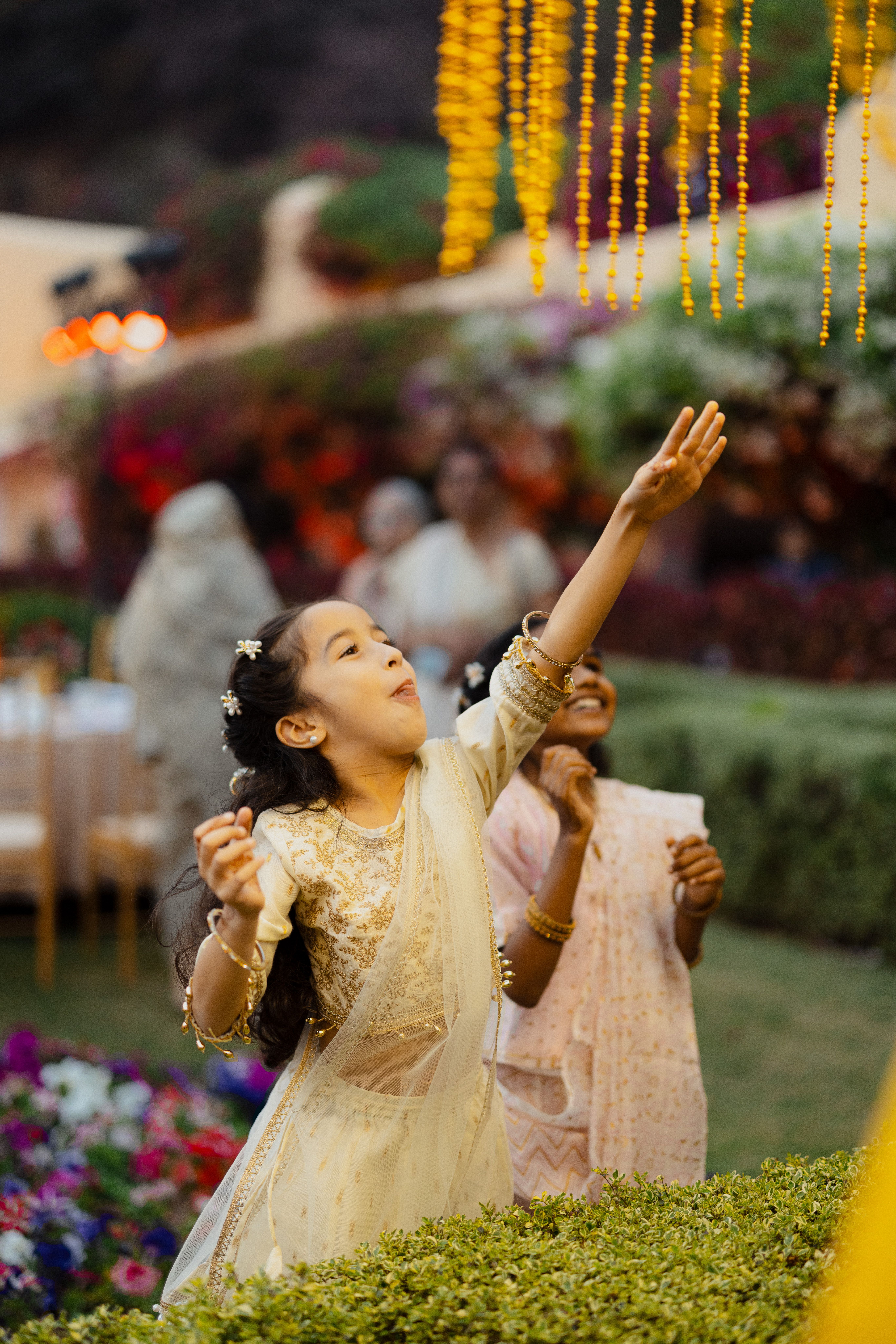 Two joyful children reaching for hanging decorations at a vibrant outdoor wedding event.