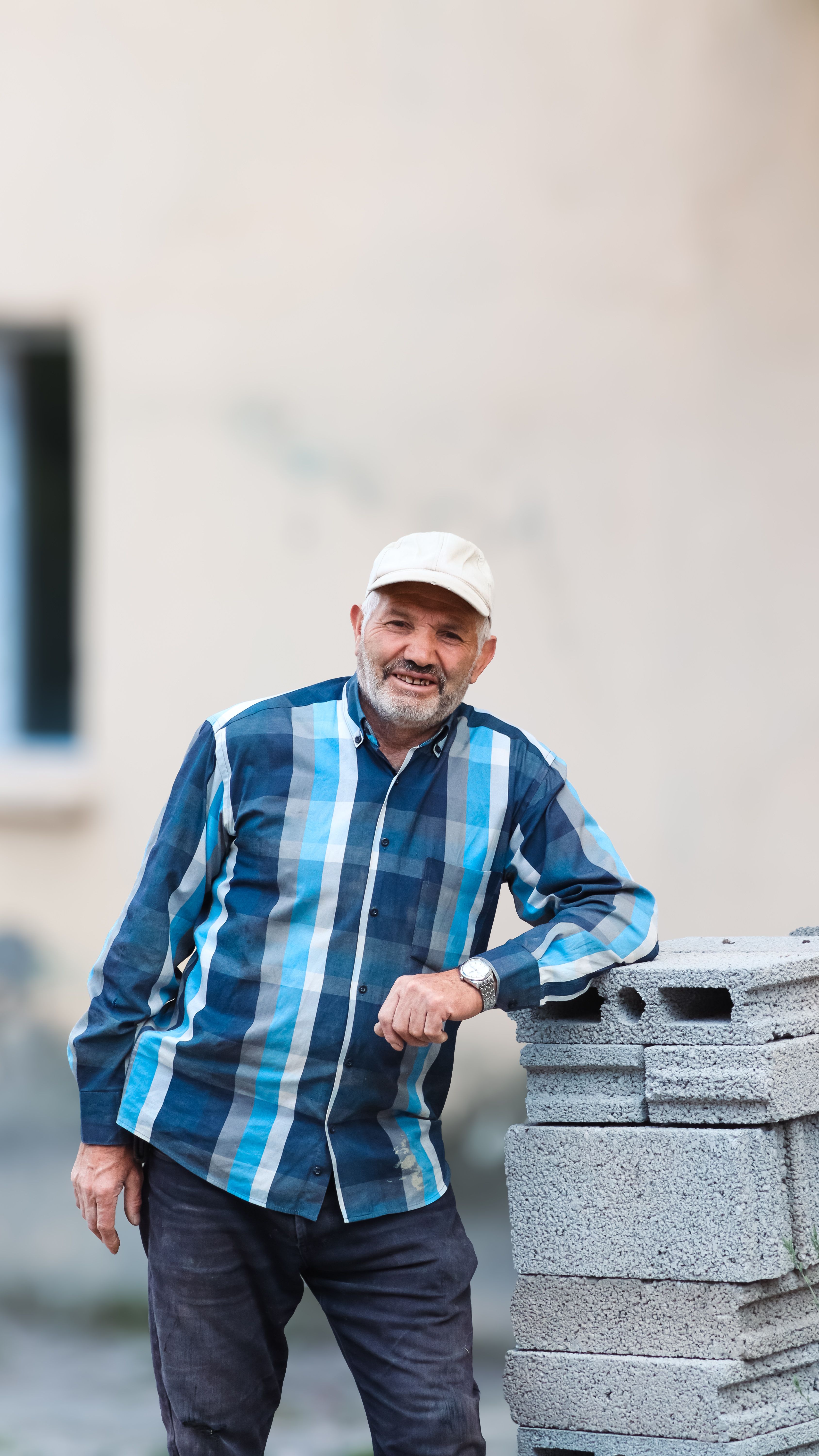 Smiling middle-aged man in casual outfit leaning on concrete blocks outdoors.