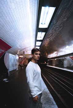 一名身穿白色毛衣的男子在空荡的地铁站台，于人造灯光下等候