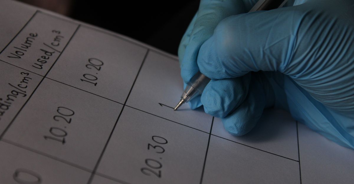Close-up of a scientist wearing blue gloves writing measurements on a data sheet.