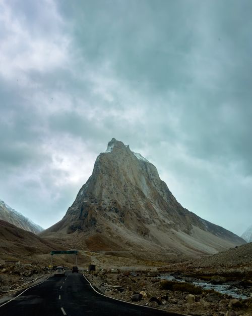 Free Dramatic view of a towering mountain peak under overcast skies with a road leading to it. Stock Photo