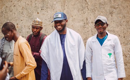Free A joyful gathering of men in traditional and modern Nigerian attire against a rustic wall. Stock Photo