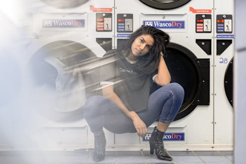 Woman in Black Shirt and Blue Denim Jeans Sitting on Front Load Washing Machine