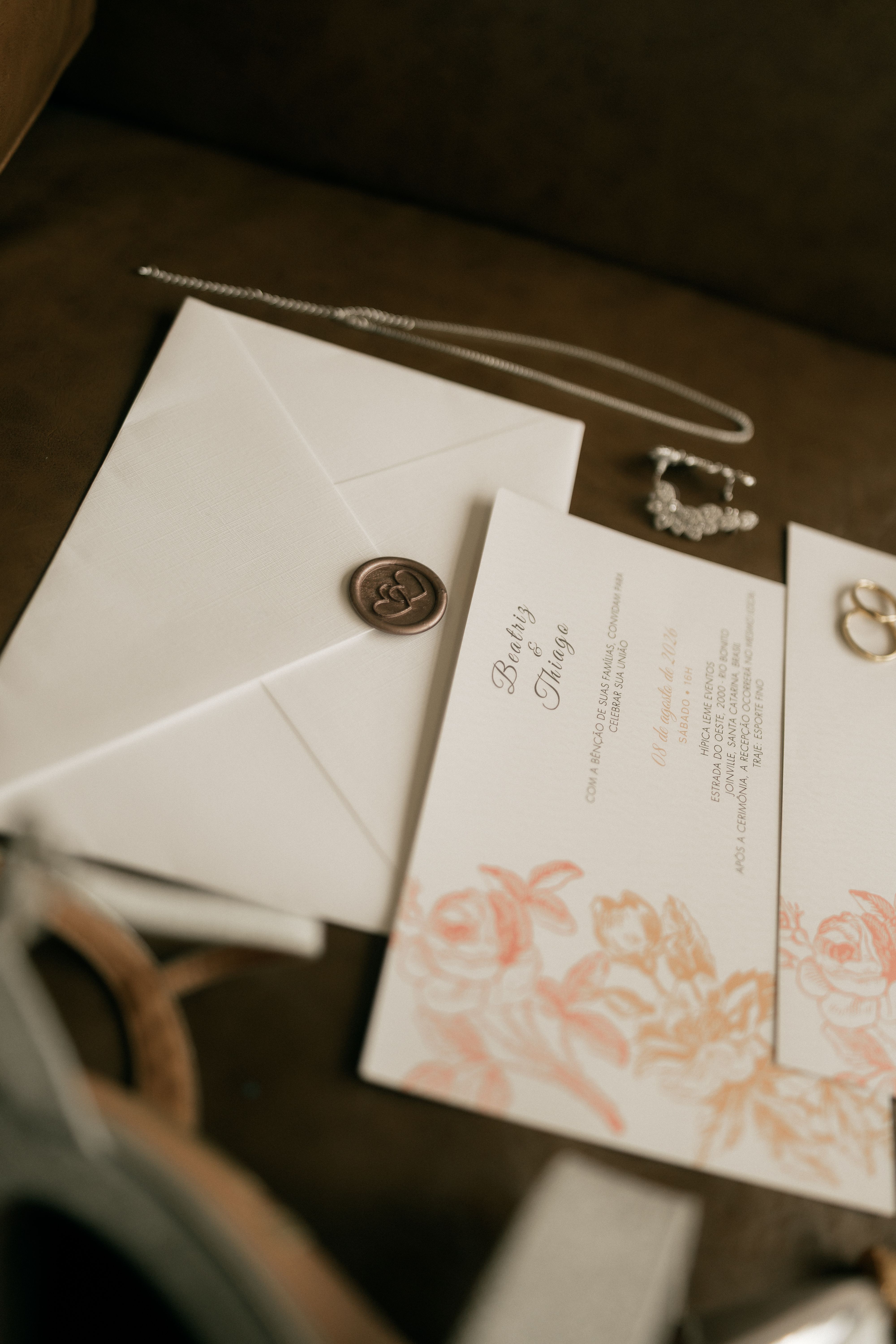 Close-up of wedding invitation, envelope, and jewelry with elegant wax seal and floral detail.