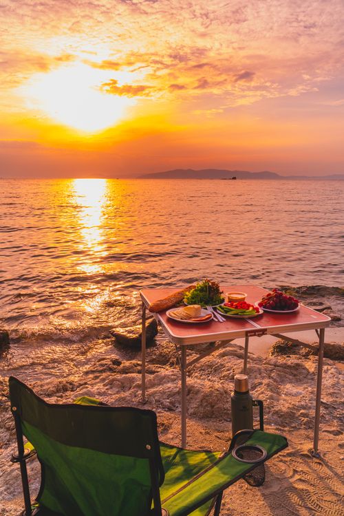 Free A picturesque beach picnic setup at sunset with vibrant sky reflections. Stock Photo