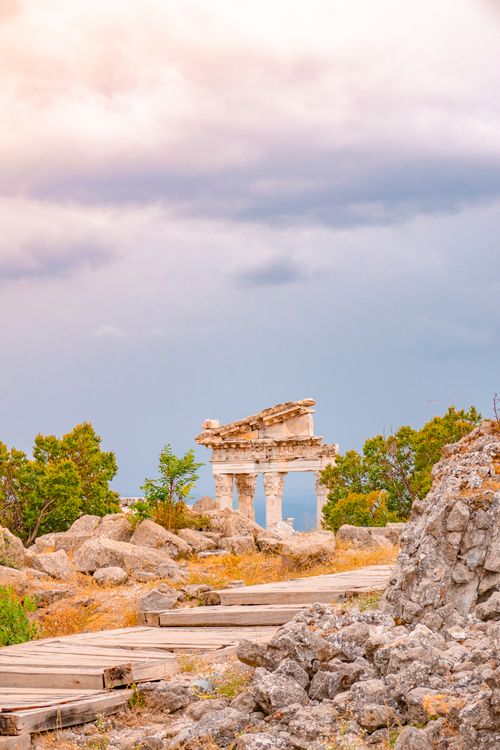Free Scenic view of ancient ruins surrounded by rocky terrain and greenery under a dramatic sky. Stock Photo