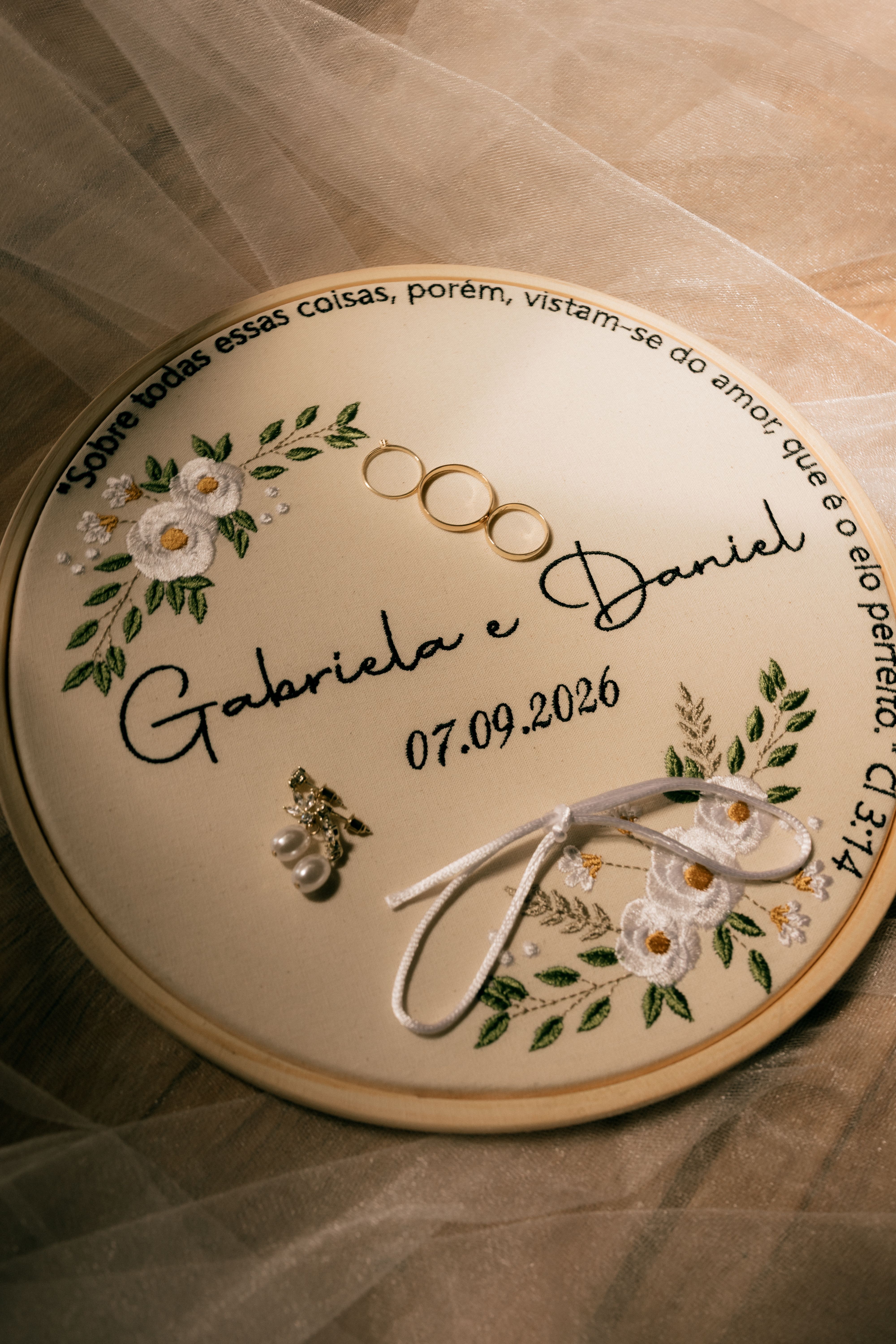 Top view of a wedding ring holder with floral embroidery and wedding rings, featuring names and date.