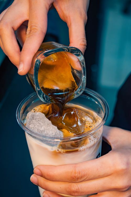 Free A close-up of hands pouring espresso into a glass of iced milk, creating an iced coffee drink. Stock Photo
